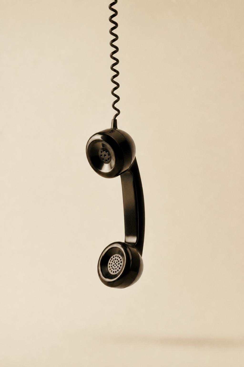 Black vintage telephone receiver suspended against a cream background